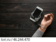Female hand in handcuffs with mobile phone on wooden background. Concept of addiction. Стоковое фото, фотограф Pixel_shot / Фотобанк Лори