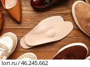 Pair of leather orthopedic insoles and different shoes on wooden background, closeup. Стоковое фото, фотограф Pixel_shot / Фотобанк Лори