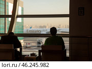 Waiting Passengers Gaze out at Emirates Plane From a Busy Airport Terminal in the Evening (2022 год). Редакционное фото, фотограф Aleksandr Golubev / Фотобанк Лори