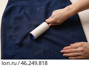Woman cleaning clothes with lint roller on light background, closeup. Стоковое фото, фотограф Pixel_shot / Фотобанк Лори