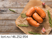 Parchment with tasty sausages on wooden table. Стоковое фото, фотограф Pixel_shot / Фотобанк Лори