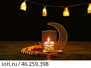 Arabic candle holder with glowing candle and tasbih on table against dark background. Стоковое фото, фотограф Pixel_shot / Фотобанк Лори