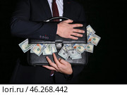 Businessman holding briefcase with dollar banknotes on dark background. Corruption concept. Стоковое фото, фотограф Pixel_shot / Фотобанк Лори