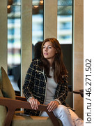 A sophisticated woman sits gracefully in a contemporary lounge, dressed in a chic ensemble. Her expression reflects contemplation as she gazes thoughtfully toward the surroundings, exuding confidence. Стоковое фото, фотограф Aleksandr Golubev / Фотобанк Лори