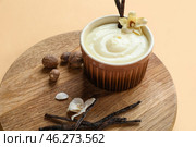 Board with ramekin of tasty pudding, vanilla sticks and nuts on beige background. Стоковое фото, фотограф Pixel_shot / Фотобанк Лори
