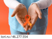 Beautiful mature female doctor with ribbon on orange background, closeup. Multiple Sclerosis Awareness Month. Стоковое фото, фотограф Pixel_shot / Фотобанк Лори