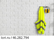 Reflective vest and hearing protectors on white brick wall. Стоковое фото, фотограф Pixel_shot / Фотобанк Лори
