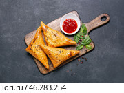 Board with tasty Uzbek samsa and tomato sauce on dark background. Стоковое фото, фотограф Pixel_shot / Фотобанк Лори