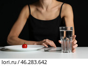 Young woman at table on dark background. Anorexia concept. Стоковое фото, фотограф Pixel_shot / Фотобанк Лори