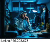 В темном офисе мужчина с арабской внешностью в традиционной одежде разговаривает по телефону. Его лицо явно сосредоточено, возможно, он замешан в телефонном мошенничестве. Стоковое AI-изображение, AI-художник Сергей Никифоров-Гордеев / Фотобанк Лори