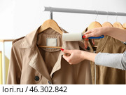 Woman cleaning coat with lint roller on light background. Стоковое фото, фотограф Pixel_shot / Фотобанк Лори