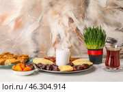 Burning candle with treats, grass and glass of tea on table near grunge wall. Novruz Bayram celebration. Стоковое фото, фотограф Pixel_shot / Фотобанк Лори
