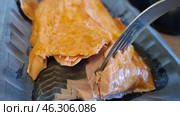 A piece of smoked fish, probably salmon or trout, in plastic packaging. The fish has a rich golden-orange hue, typical of smoking. You can see layers of tender and juicy fillet, which are easily separated by a fork. The shiny surface indicates the oily structure of the product. This delicacy is often served as an appetizer, used in sandwiches or salads. Стоковое фото, фотограф Анна Кривицкая / Фотобанк Лори