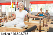 Senior woman performs exercise on reformer to improve coordination, balance, and posture. Стоковое фото, фотограф Яков Филимонов / Фотобанк Лори