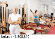 Positive senior woman coach stands in large gym against background of Pilates simulators. Стоковое фото, фотограф Яков Филимонов / Фотобанк Лори