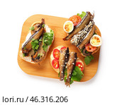 Wooden board of tasty sandwiches with canned smoked sprats on white background. Стоковое фото, фотограф Pixel_shot / Фотобанк Лори