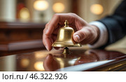 Elegant brass bell being rung by a hand in a luxurious hotel lobby during daytime service. Стоковое AI-изображение, AI-художник Сергей Толмачёв / Фотобанк Лори