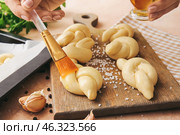 Woman greasing uncooked garlic buns with oil on color background. Стоковое фото, фотограф Pixel_shot / Фотобанк Лори