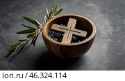 Religion, faith, liturgy, Ash Wednesday. Great lent. A wooden cross, a ceremonial bowl made of ash and an olive branch on a gray background. Стоковое AI-изображение, AI-художник Photojuli / Фотобанк Лори