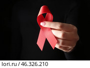 Female hand with red ribbon on dark background. AID awareness concept. Стоковое фото, фотограф Pixel_shot / Фотобанк Лори
