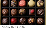 A box of exquisite chocolates, each of which is unique in its design and composition. The assortment includes chocolate truffles, pralines, ganache and other sweets decorated with nuts, berries, glaze and sprinkles. In the center of the composition are sweets with raspberries, caramelized nuts and golden powder. The visual variety of shapes, colors and textures makes the image especially attractive. Стоковое AI-изображение, AI-художник Анна Кривицкая / Фотобанк Лори