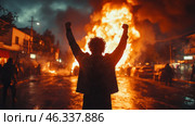 A scene of unrest, protest or revolutionary uprising. In the center of the frame is a man in a jacket, standing with his back to the viewer, with his fists raised in the air, symbolizing victory, a challenge to the system or an act of resistance. In the background, cars or barricades are burning, the fire illuminates the street, creating an atmosphere of chaos and tension. Around him are blurred silhouettes of other people, which adds dynamism and drama to the scene. Стоковое AI-изображение, AI-художник Анна Кривицкая / Фотобанк Лори