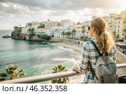 A girl traveler with a backpack on the background of the southern coast of the sea. A woman travels, enjoys life and the environment. Tourism. Стоковое AI-изображение, AI-художник Photojuli / Фотобанк Лори
