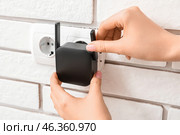 Woman plugging black WiFi repeater in electric socket on white brick wall. Стоковое фото, фотограф Pixel_shot / Фотобанк Лори