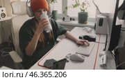 Young gamer enthusiastically engaged at their desk while wearing headphones in modern workspace. Focused gamer in stylish headphones and trendy beanie, immersed in gaming at sleek desk setup. Стоковое видео, видеограф Енваев Андрей / Фотобанк Лори