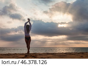 Standing on the golden sands, a figure stretches towards the sky as the sun sets behind the clouds. Gentle waves lap at the shore, creating a peaceful atmosphere in Sri Lanka's beautiful outdoors. Стоковое фото, фотограф Aleksandr Golubev / Фотобанк Лори