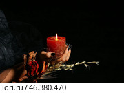 Witch holding dried flowers and burning candle for ritual on black background. Стоковое фото, фотограф Pixel_shot / Фотобанк Лори