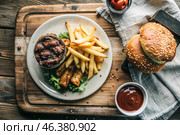 French fries, burger, pork ribs on a stylish board on a wooden background. Fried potatoes. The concept of fast food, junk food and fast food preparation. Стоковое AI-изображение, AI-художник Photojuli / Фотобанк Лори