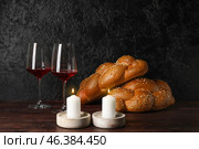 Glowing candles with traditional challah bread and wine on dark background. Shabbat Shalom. Стоковое фото, фотограф Pixel_shot / Фотобанк Лори