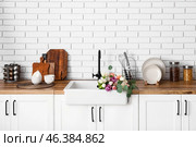 Sink with beautiful flowers and kitchen utensils on counters near white brick wall. Стоковое фото, фотограф Pixel_shot / Фотобанк Лори