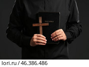 Young priest with Bible and cross on dark background. Стоковое фото, фотограф Pixel_shot / Фотобанк Лори