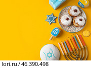 Menorah, dreidels, kipa, plate with donuts and gift box for Hanukkah celebration on yellow background. Стоковое фото, фотограф Pixel_shot / Фотобанк Лори