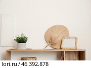 Shelving unit with houseplant, bamboo fan and photo frame near white wall in living room. Стоковое фото, фотограф Pixel_shot / Фотобанк Лори