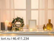 Christmas wreath with candles, frame, decor and glowing lights on mantelpiece near window. Стоковое фото, фотограф Pixel_shot / Фотобанк Лори
