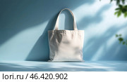 Stylish white tote bag standing against a light blue background with soft shadows, perfect for casual outings and eco-friendly shopping. Стоковое AI-изображение, AI-художник Сергей Толмачёв / Фотобанк Лори
