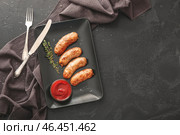 Тарелка с вкусными жареными колбасками и соусом на темном фоне. Стоковое фото, фотограф Pixel_shot / Фотобанк Лори