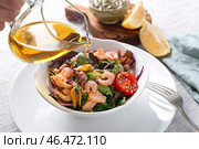 Женщина наливает оливковое масло в миску с вкусным салатом из морепродуктов на деревянном столе. Стоковое фото, фотограф Pixel_shot / Фотобанк Лори