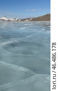 Vertical video of winter landscape of frozen Baikal lake on cold sunny day in February. Snow-capped hills frame iced bay with blue ice surface with cracks in mouth of Anga River. Стоковое видео, видеограф Виктория Катьянова / Фотобанк Лори