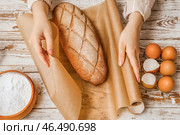 Женщина заворачивает свежий хлеб в бумагу для выпечки на белом деревянном фоне, крупным планом. Стоковое фото, фотограф Pixel_shot / Фотобанк Лори