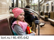 In a quiet subway car, a cheerful five-year-old girl in a pink hat enjoys her journey. Clutching a colorful toy, she gazes around, embracing the excitement of the ride indoors. Стоковое фото, фотограф Aleksandr Golubev / Фотобанк Лори