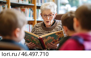 Senior librarian reading a story to children in the library. Стоковое AI-изображение, AI-художник Юрий Поздников / Фотобанк Лори