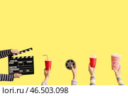Множество рук с кинематографическим хлопушкой, ведром попкорна и напитками на желтом фоне. Стоковое фото, фотограф Pixel_shot / Фотобанк Лори
