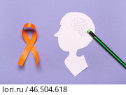 Голова человека из бумаги и оранжевая лента на сиреневом фоне. Месяц осведомленности о рассеянном склерозе. Стоковое фото, фотограф Pixel_shot / Фотобанк Лори