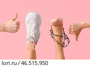 Женские ноги с поднятым большим пальцем для кроссовка и опущенным для обуви в колючей проволоке на розовом фоне. Концепция неудобной обуви. Стоковое фото, фотограф Pixel_shot / Фотобанк Лори