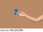 Женская рука с синей лентой на бежевом фоне. Концепция осведомленности о раке толстой кишки. Стоковое фото, фотограф Pixel_shot / Фотобанк Лори