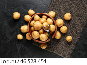 Деревянная миска с сырыми картофелинами и овощечистка на черном фоне. Стоковое фото, фотограф Pixel_shot / Фотобанк Лори
